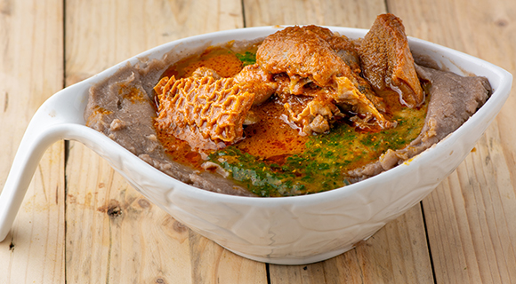 a beef nigerian soup being served a white ceramic bowl on a natural wooden table 